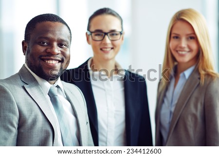 Smiling and confident businessman with two female colleagues on background