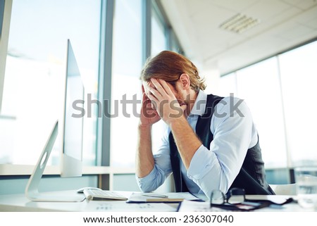 Tired businessman touching his head while looking at monitor in office