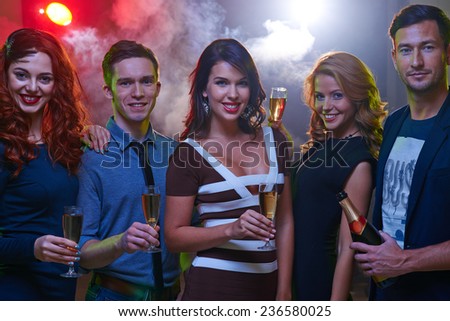 Group of happy guys and girls toasting at party in night club