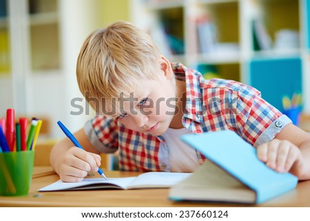 Dishonest schoolboy looking the answer in book at lesson