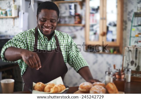 Happy young man powdering buns with vanilla sugar in bakery shop