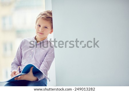 Handsome schoolboy with exercise-book looking at camera