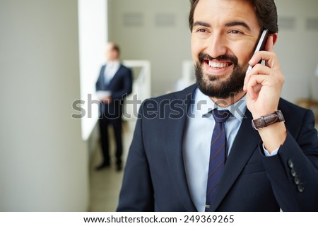 Young businessman speaking on the phone on background of his colleague in office