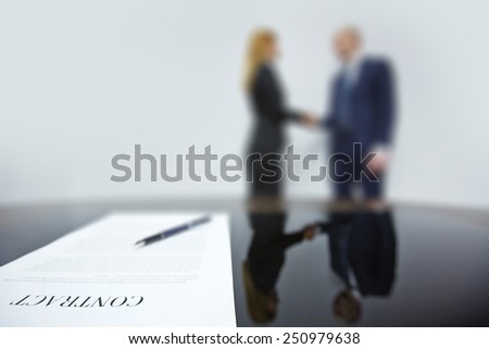 Business contract with pen on background of co-workers handshaking