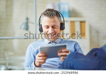 Happy businessman with earphones using touchpad