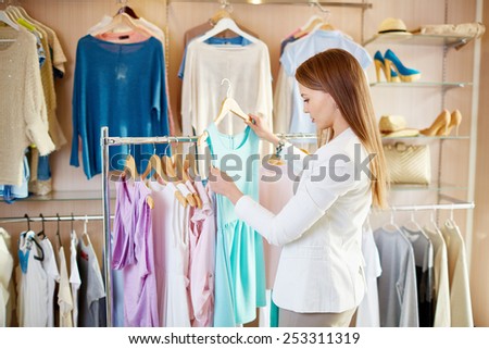 Beautiful young shopper choosing dress in boutique