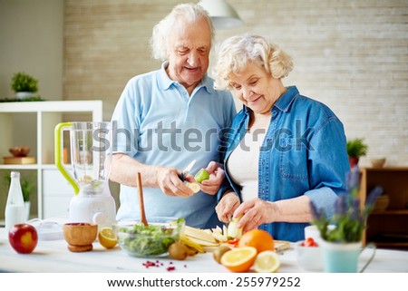 Modern senior couple preparing fresh fruits for making smoothie
