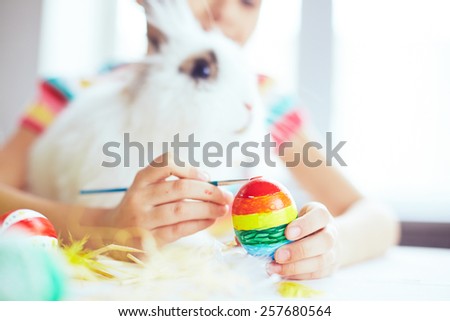 Girl painting an egg and embracing Easter rabbit