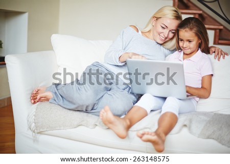 Mother pointing to computer and daughter looking at laptop and smiling