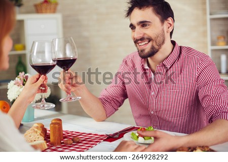 Happy young man with glass of red wine toasting with his wife