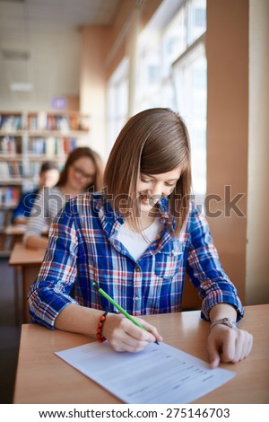 Happy girl filling in gaps in test form at lesson in college