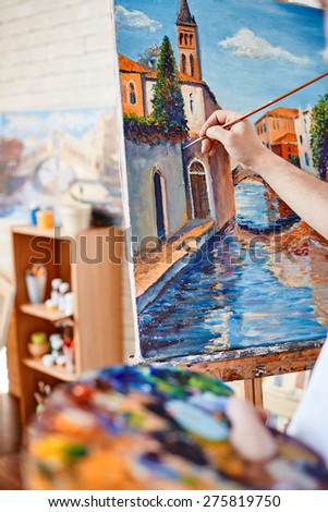 Hand of artist painting street of Venice on canvas
