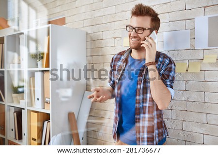 Young businessman standing by office wall and speaking on the cellphone