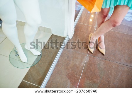 Legs of a shopper standing on the floor and those of mannequin in the shop window