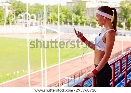 Sporty girl with earphones and iphone visiting stadium