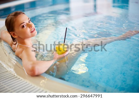 Young female in bikini holding glass of juice while relaxing in swimming pool