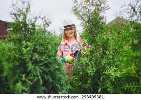 Happy female gardener looking at camera while taking care of thuja