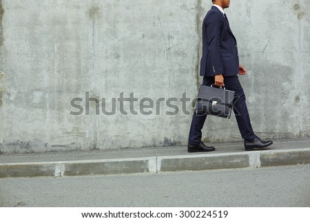 Modern businessman with briefcase walking along concrete wall