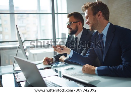 Confident businessman consulting his colleague and pointing at computer monitor at meeting