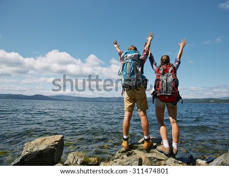 Couple of travelers with raised arms enjoying summer vacation by the sea