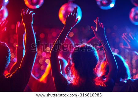 Group of young people with raised arms dancing in night club