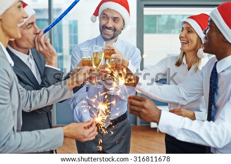 Happy colleagues in Santa caps having Christmas fun while toasting with champagne at party in office