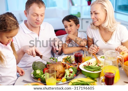 Happy young family sitting by festive table and eating traditional Thanksgiving food