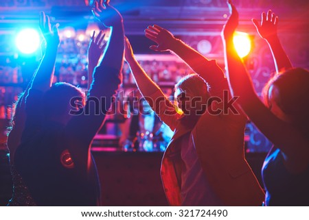 Happy friends with raised arms dancing at night club