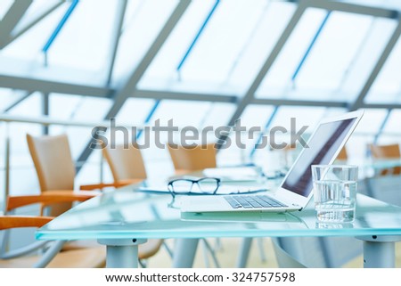 Laptop and glass of water on workplace in empty conference hall