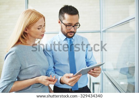 Two confident colleagues with touchpad looking at data at meeting