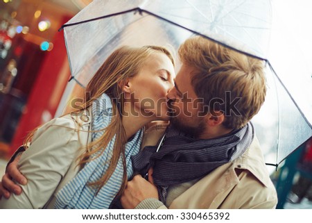 Amorous young couple kissing under umbrella