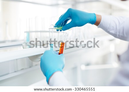 Gloved hands of chemist mixing up fluids