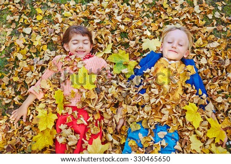 Happy friends with closed eyes lying in dry autumn leaves