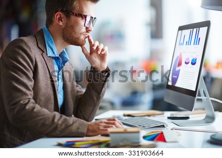 Young pensive businessman in eyeglasses working in office