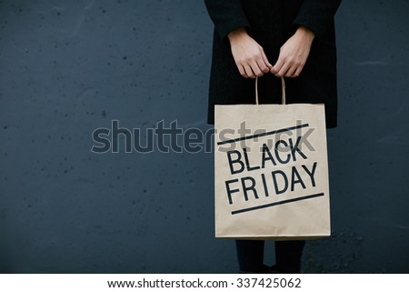Young woman in black holding paperbag with note Black Friday