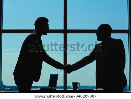 Outlines of two businessmen handshaking against window