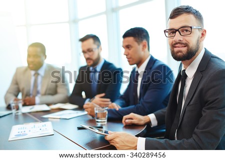 Happy businessman looking at camera at conference with colleagues on background