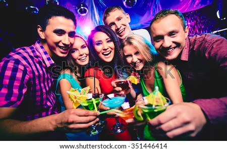 Joyful group of friends toasting with cocktails at party