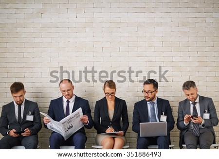 Elegant young people looking for jobs while sitting along brick wall