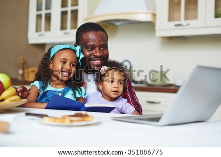 Happy young man with two daughters watching cartoons in the kitchen