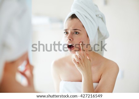Young woman noticing a pimple on her face in terror