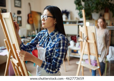 Serious young woman painting at art studio