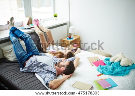 High angle of father lying relaxing on bed with his daughter, feet up on windowsill, both looking up, dreaming and talking