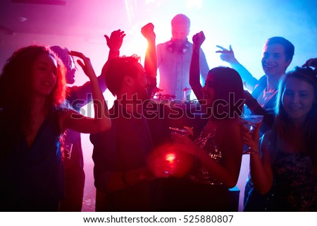 Young couple with drinks and their friends dancing at night party