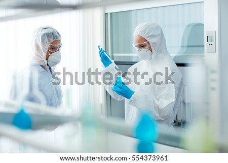 Two students of chemical faculty in protective overalls testing toxic liquid substance in flask