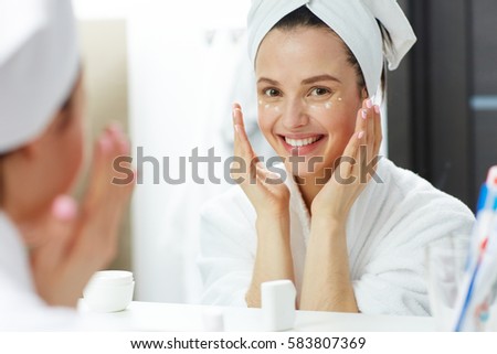 Happy woman with toothy smile pampering eye-cream