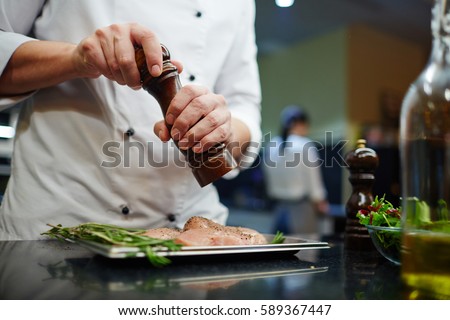Man in uniform of chef seasoning lean meat with spices