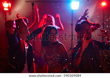 Happy male and female students dancing at graduation party with loud pop music and shining confetti