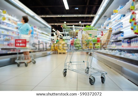 Shopping cart full of grocery standing next to shelves with dairy products in hypermarket