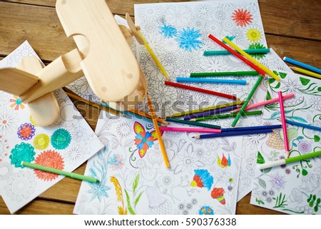 Pencils, felt-tip pens, pages from coloring books, toy plane located on wooden table, high angle view